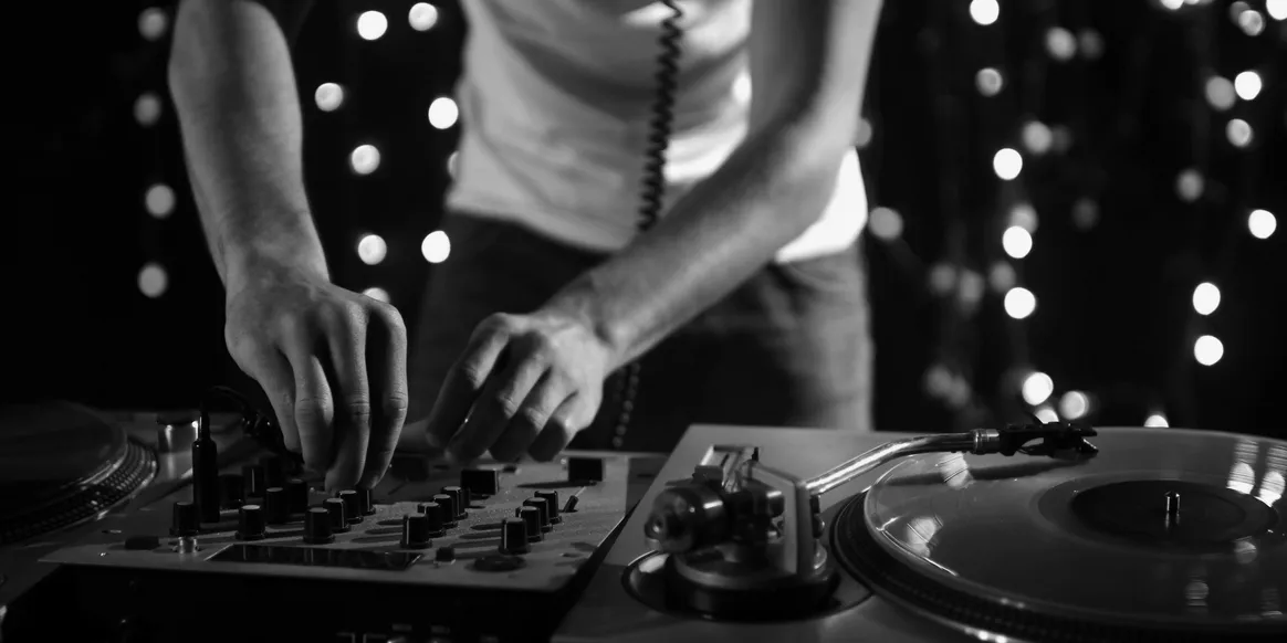Hands working a DJ mixer and turntable in front of soft party lights