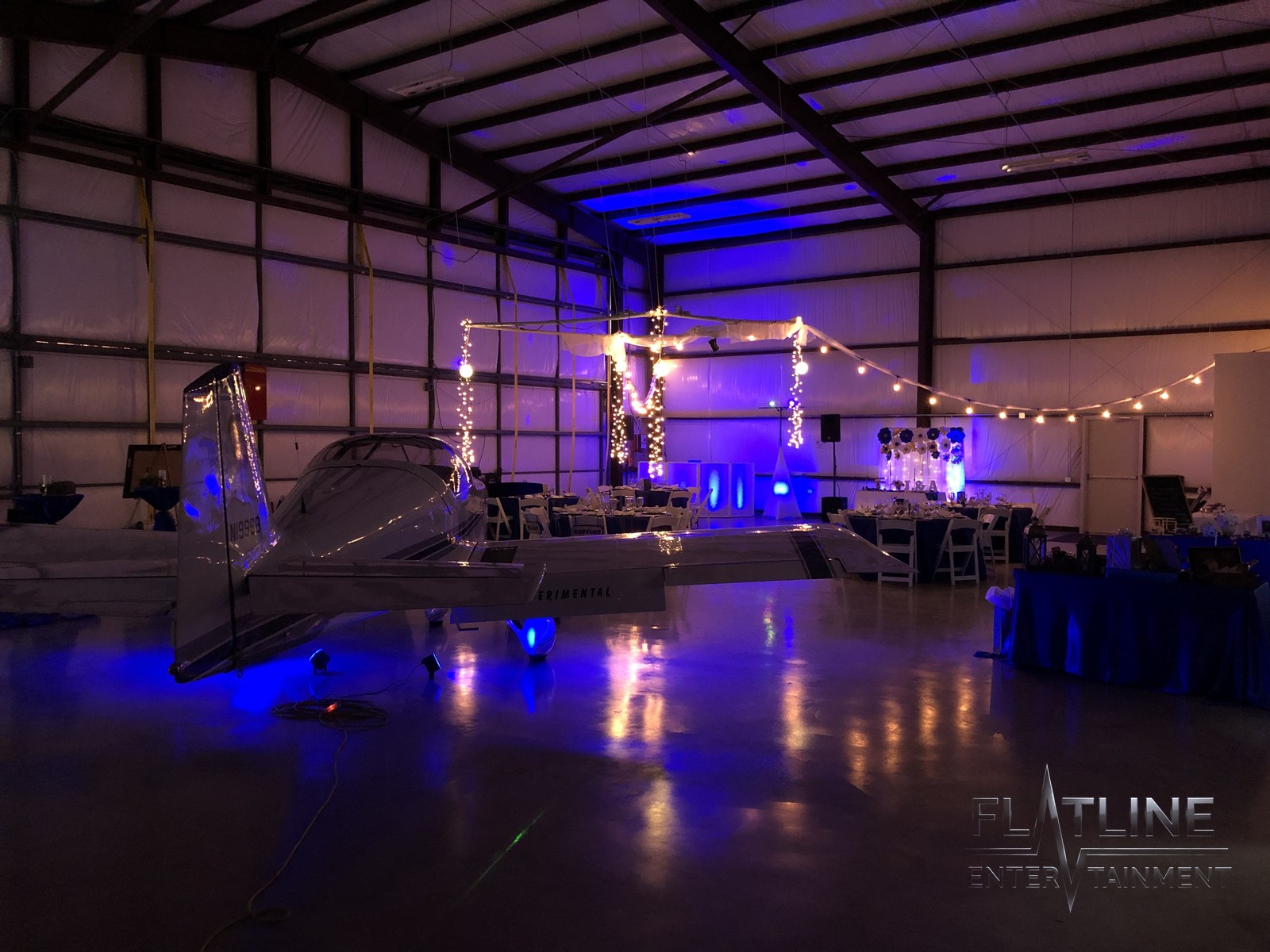 A wedding reception room with the Flatline DJ booth, blue uplighting, and an open dance floor