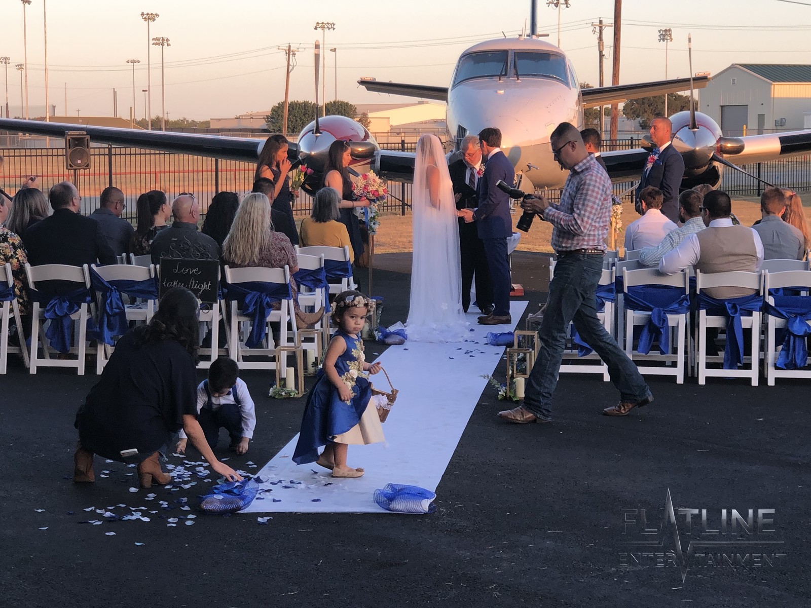 An outdoor wedding ceremony in front of a private jet at sunset, with guests seated along the aisle